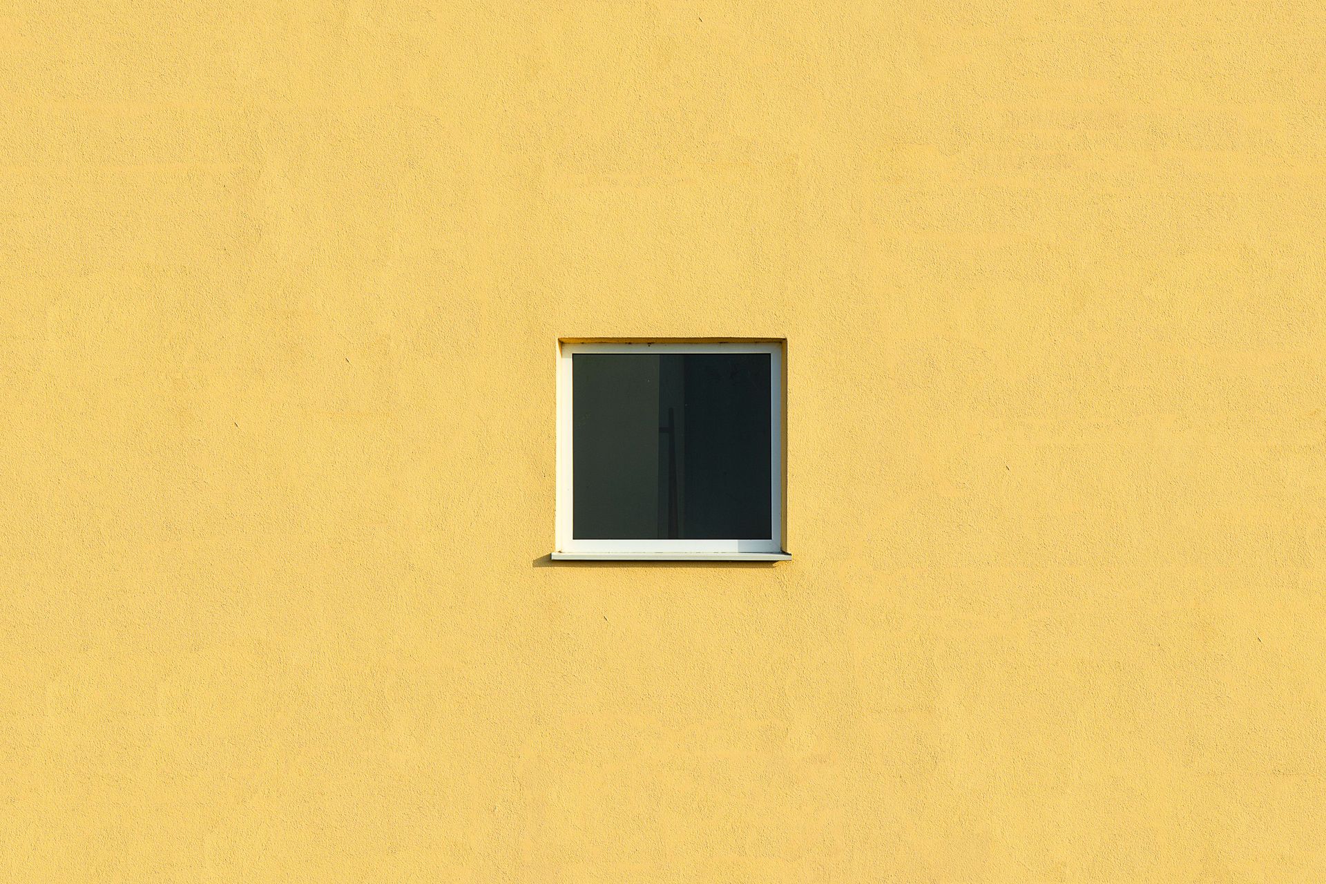 A small isolated window on a vibrant yellow wall offers minimalist architectural design.